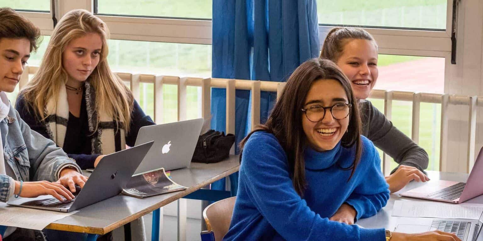 Focused diverse students using laptops during a classroom lesson at an international school.