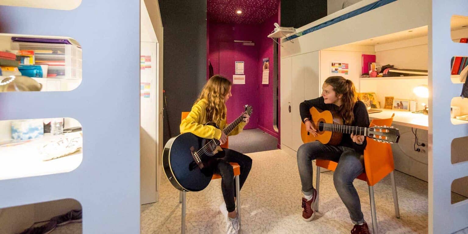Young girls playing guitars in a cozy, brightly lit school music room for an engaging learning environment.