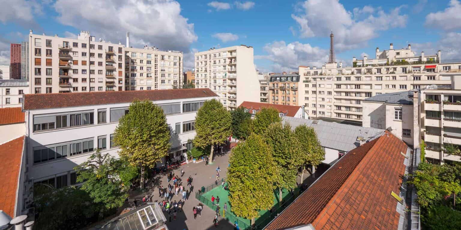 Bright Parisian school courtyard with students, surrounded by mid-rise residential buildings and iconic Eiffel Tower in background.