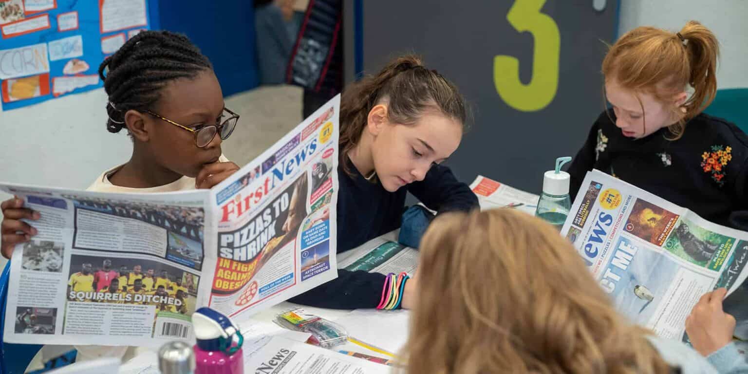 Focused students reading newspapers at school, promoting literacy and engagement in educational activities.