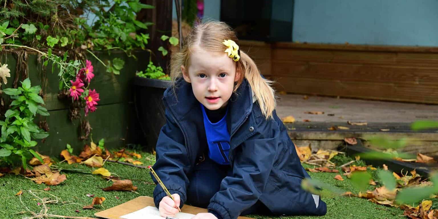 Preschool girl drawing outdoors in a garden setting, fostering creativity and learning at a world school.