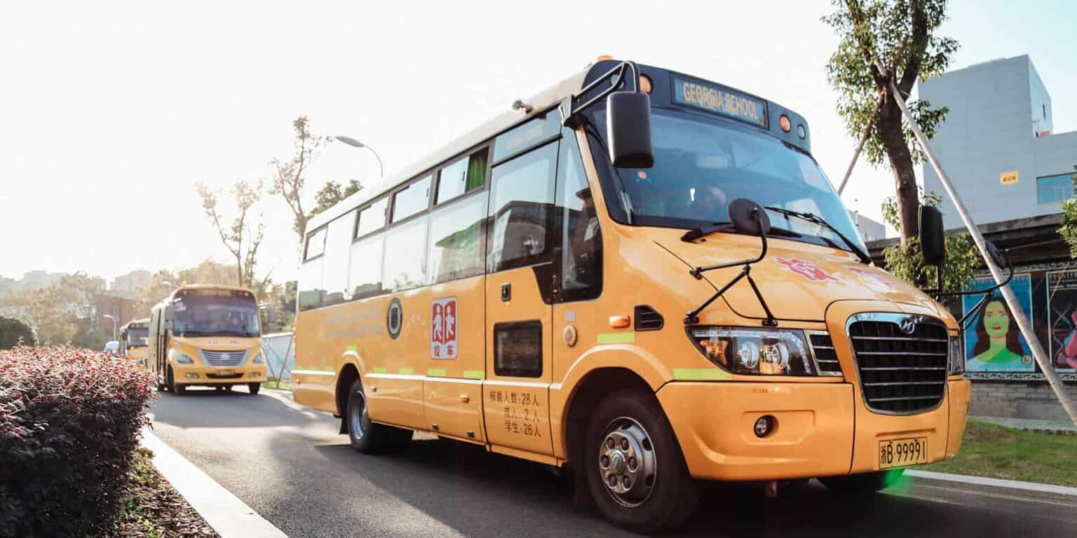 Yellow school bus in front of a school, emphasizing safe student transportation | Image of school buses transporting students to World Schools.