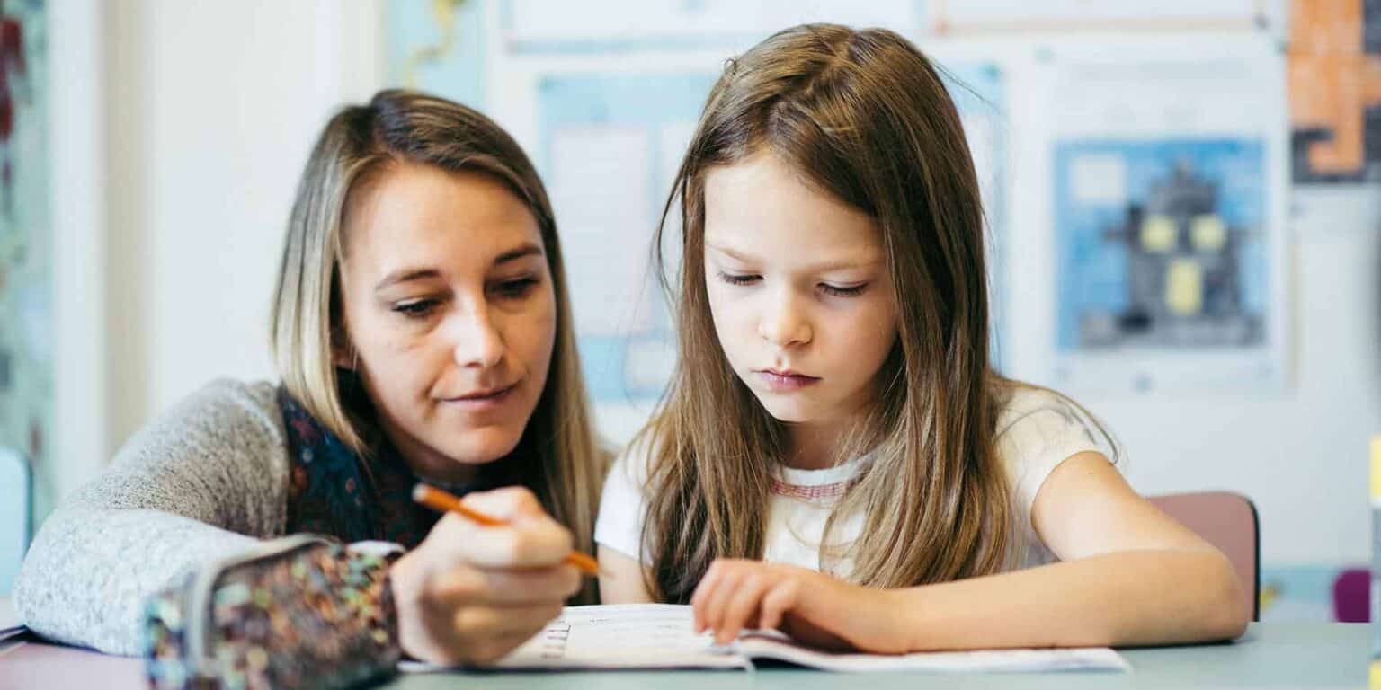 Focused teacher helping young girl with homework in classroom, studying at school, educational support, student learning, World Schools.