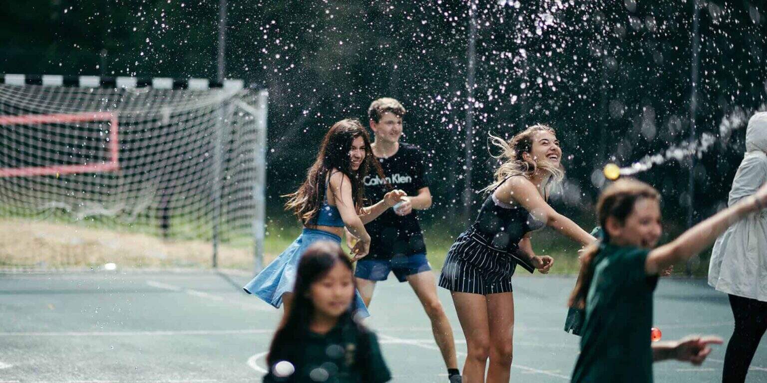 Joyful children playing with water on a school sports field, promoting active learning and outdoor activities.