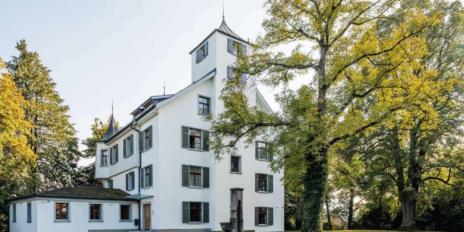 Charming white school building surrounded by green trees, showcasing a peaceful learning environment.