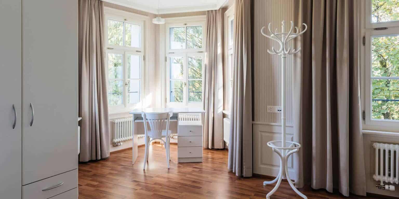 Bright study room with large windows, white furniture, and natural wooden flooring, ideal for a comfortable learning environment.