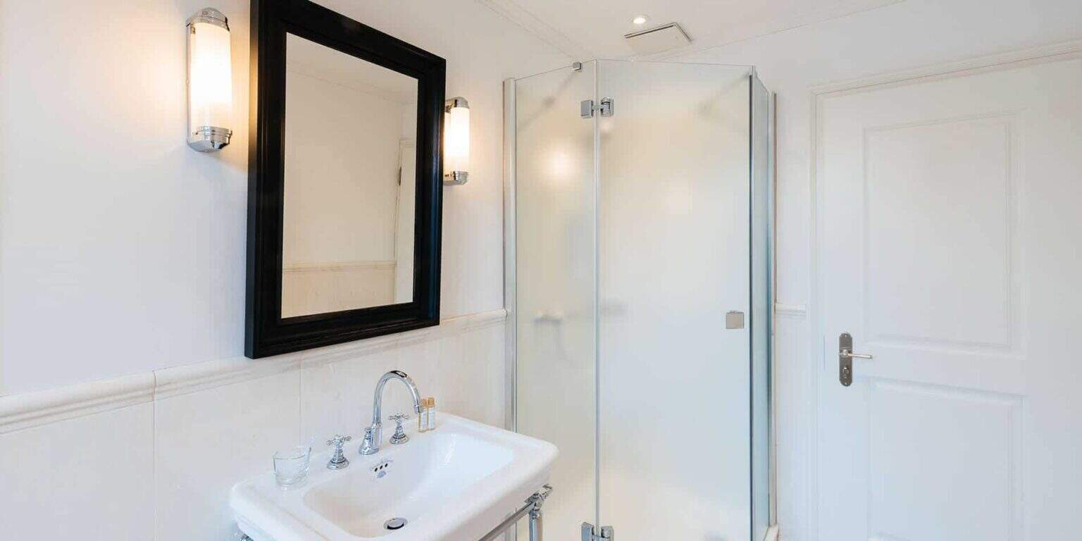 Bright modern bathroom with white walls, black-framed mirror, and sleek shower enclosure.