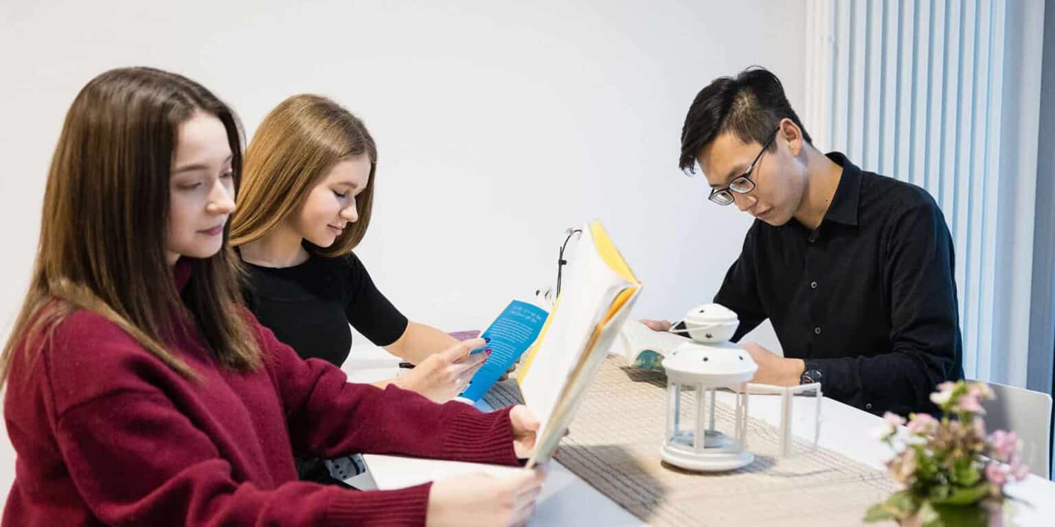 Students reading books at a modern classroom with educational materials and an indoor plant for a productive learning environment.