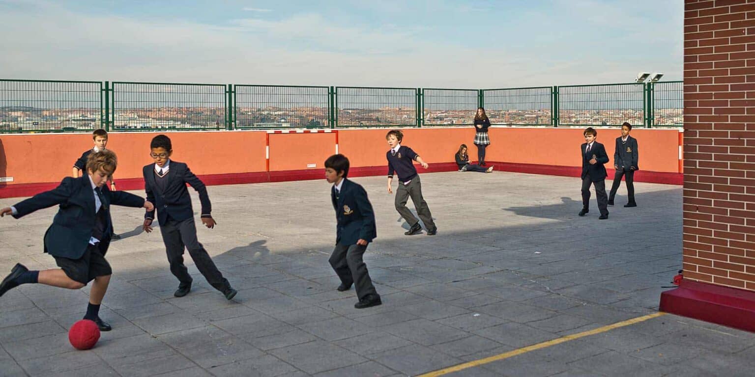 Students playing soccer on a school rooftop playground with cityscape in the background.