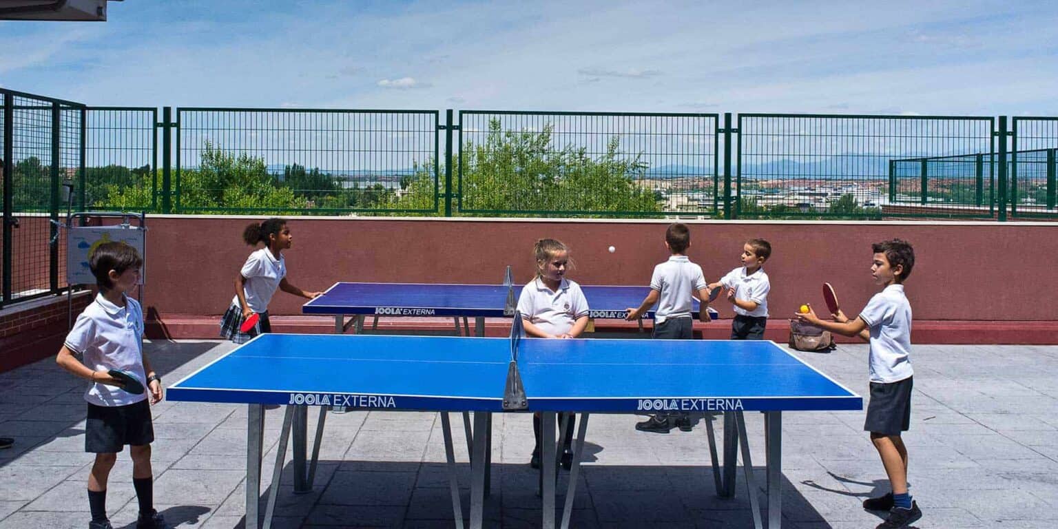 Kids playing table tennis outdoors at a school campus with a scenic city view, emphasizing sports and extracurricular activities at World Schools.