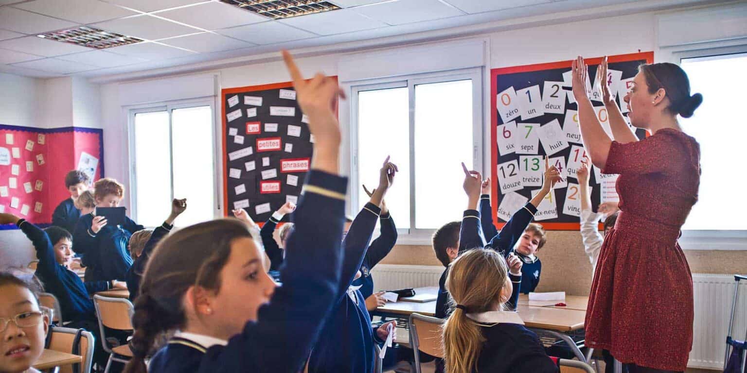Children raising hands in classroom during an interactive lesson at a World Schools international school.