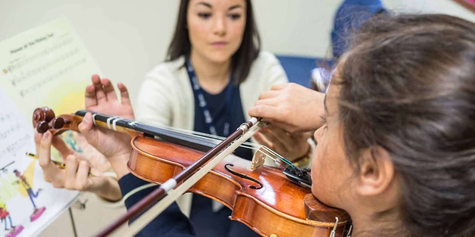 Junior violin student receiving guidance in music school, focusing on skill development and performance.