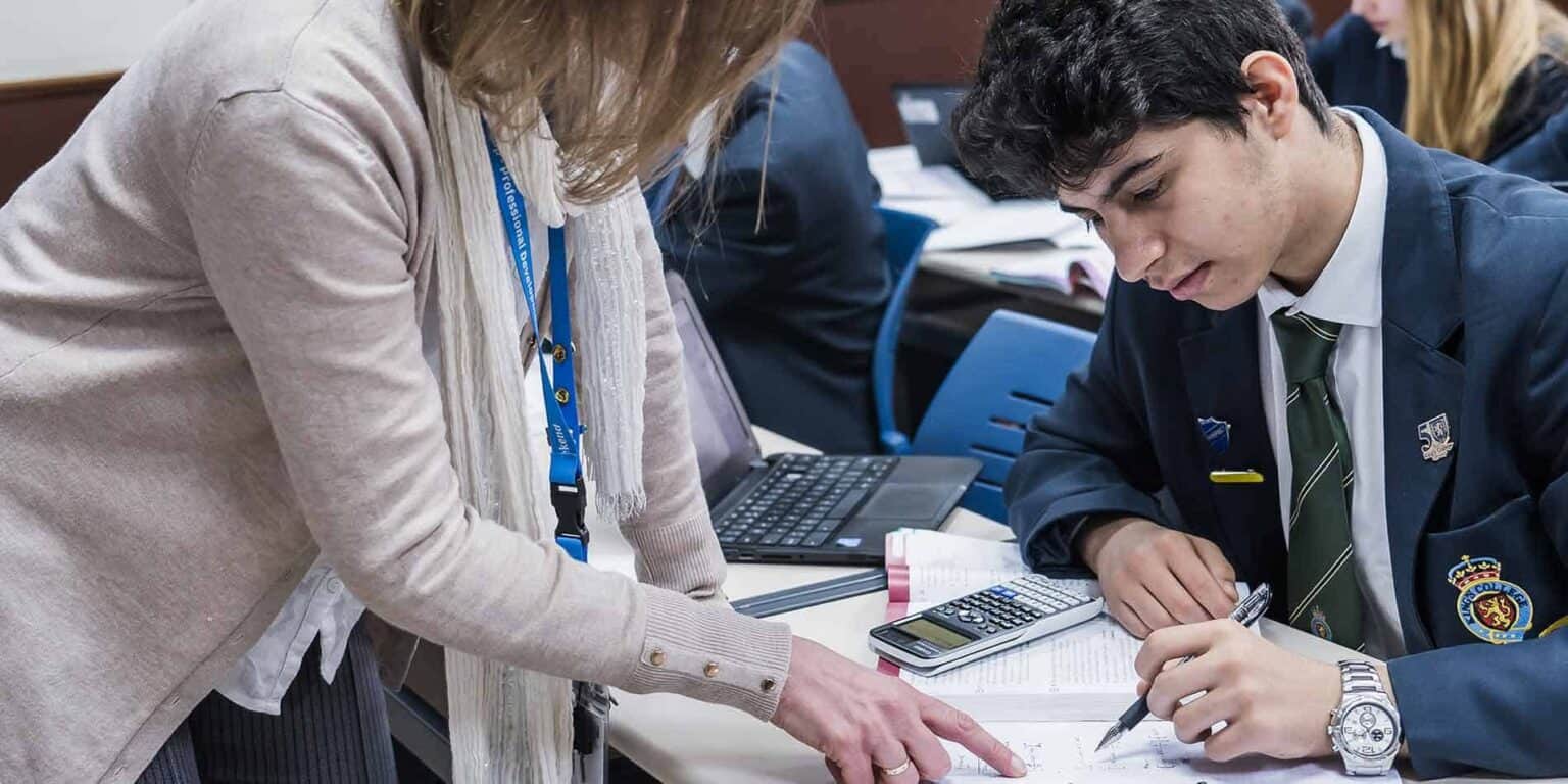 Focused student working with teacher in classroom, using calculator and notes for math lesson.