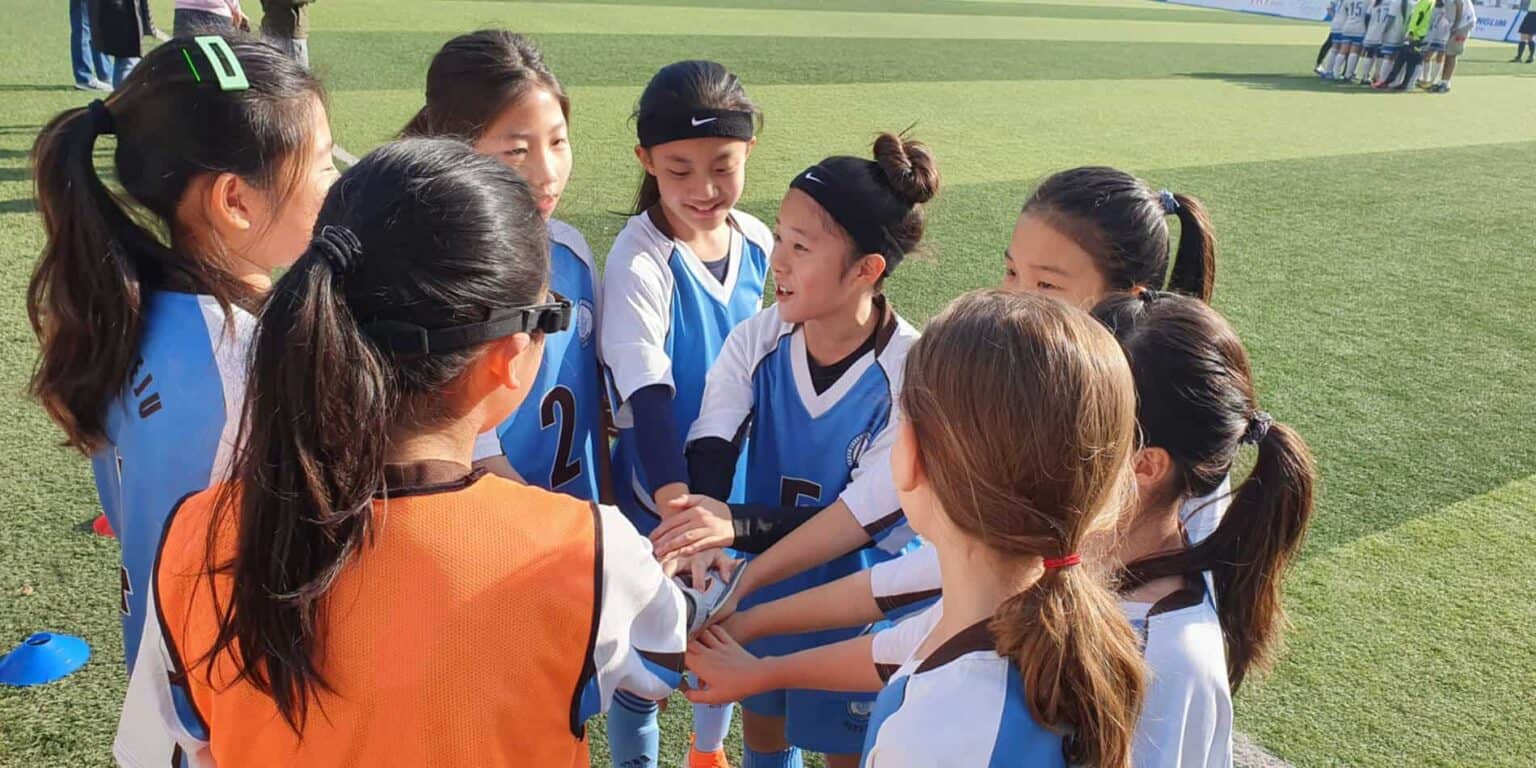 Girls' soccer team huddle during a sports match for schoolgirls at an international school event.