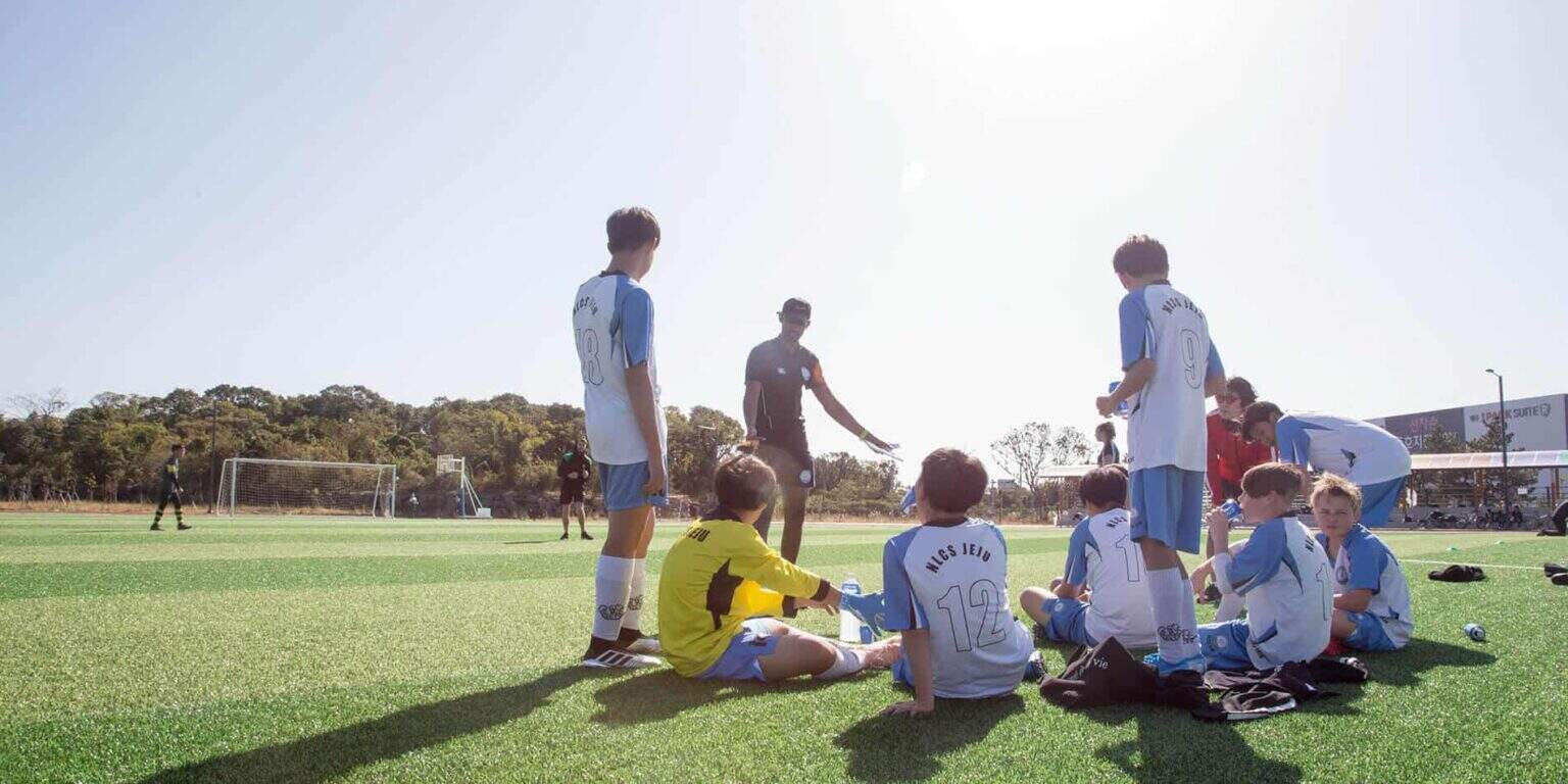 Young soccer players receiving coaching during a team practice session at an international school's sports field.