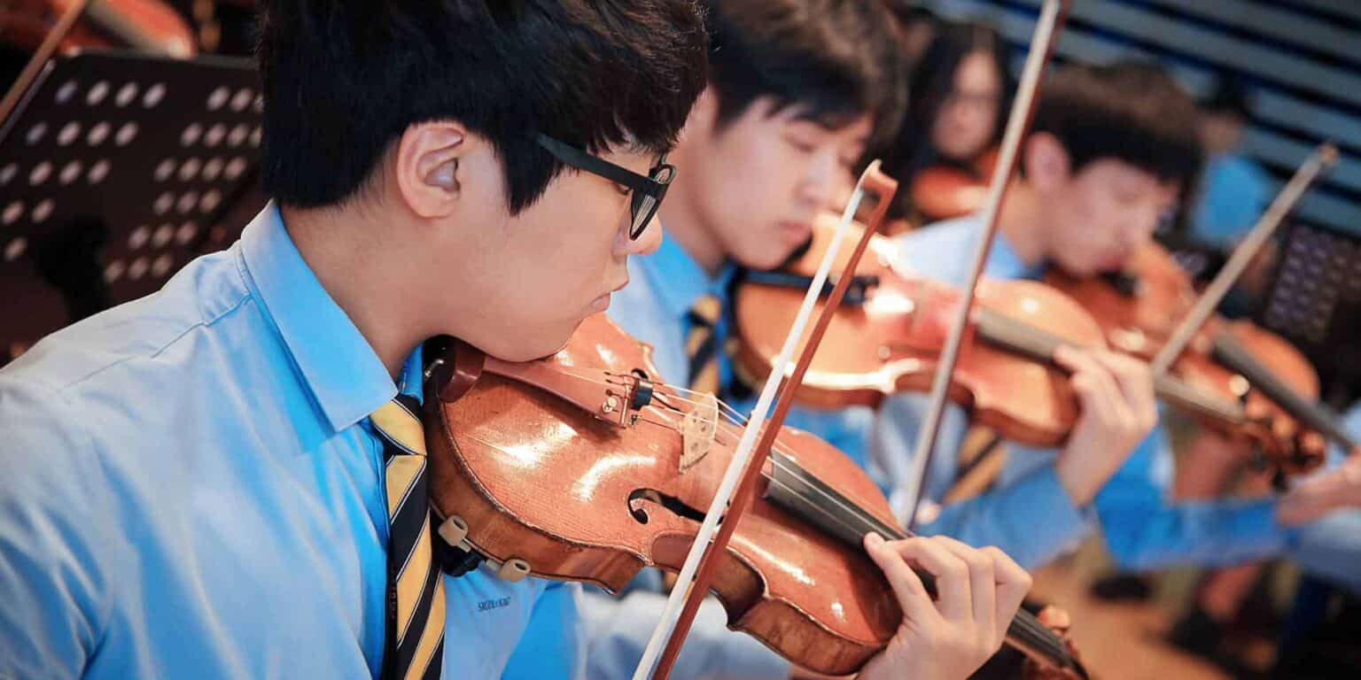 Young male student playing violin in orchestra, focus on music education.