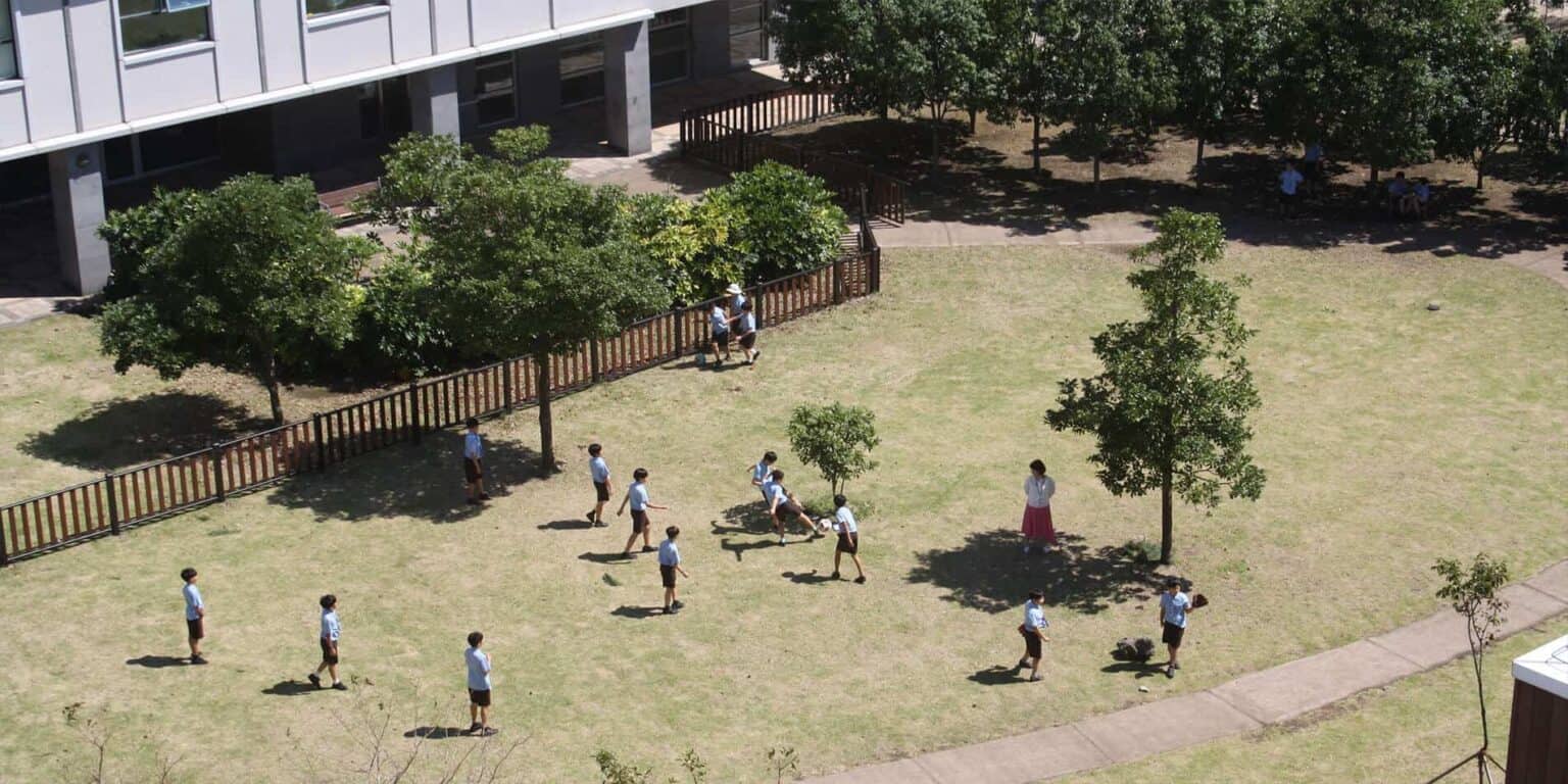Students playing outside at a modern school campus with green trees and open grassy areas.