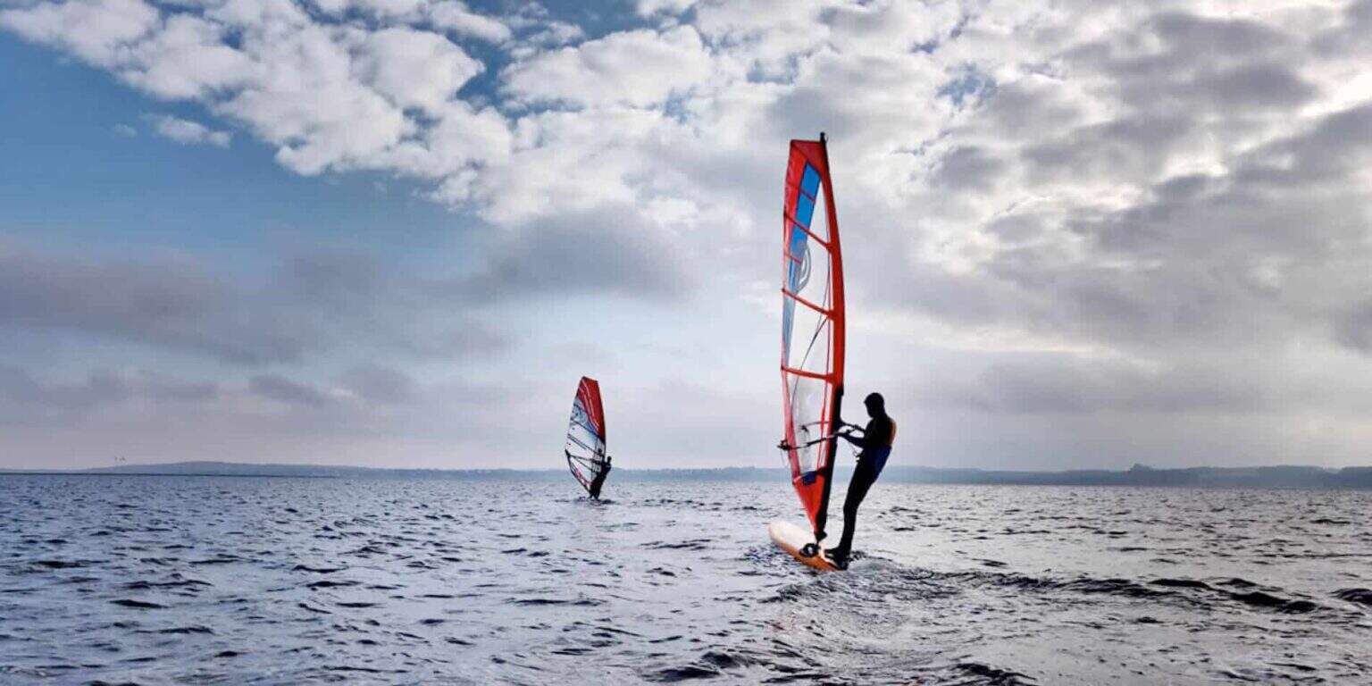 Vibrant windsurfing on open water with cloudy sky, showcasing adventure and water sports.