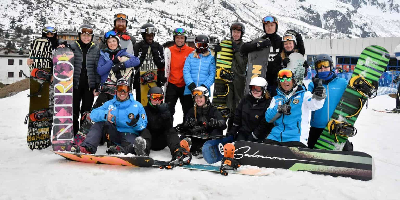 Active group of students and instructors on a snowy mountain with snowboards and ski gear for an outdoor winter sports lesson.