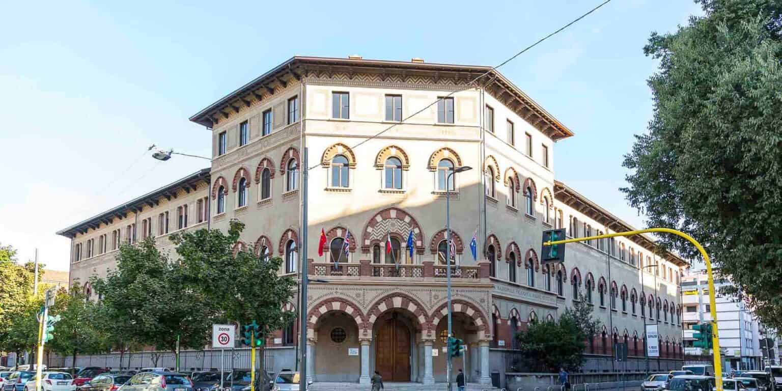 Historic European school building with flags, trees, and busy street scene, in vibrant city setting.