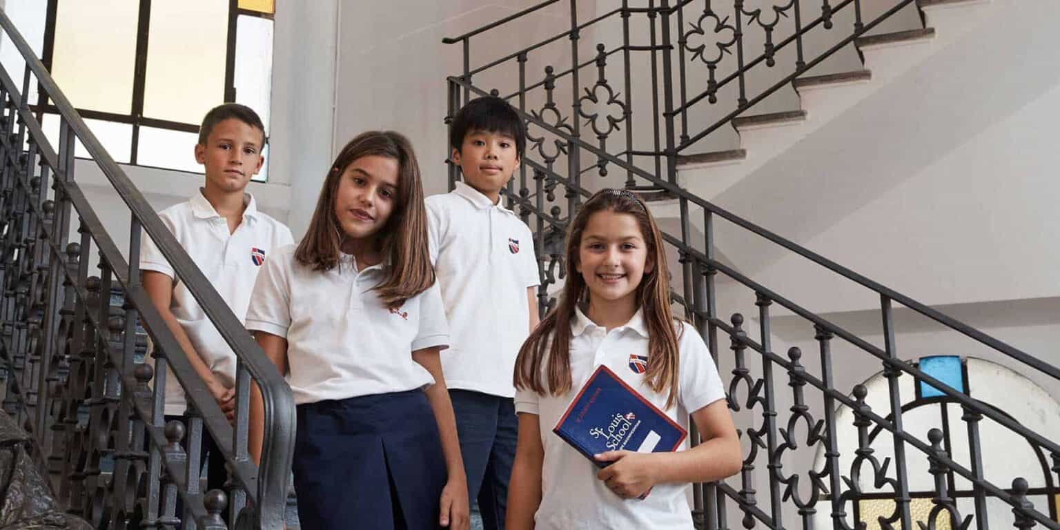 Bright young students in school uniforms standing on staircase at World Schools campus.