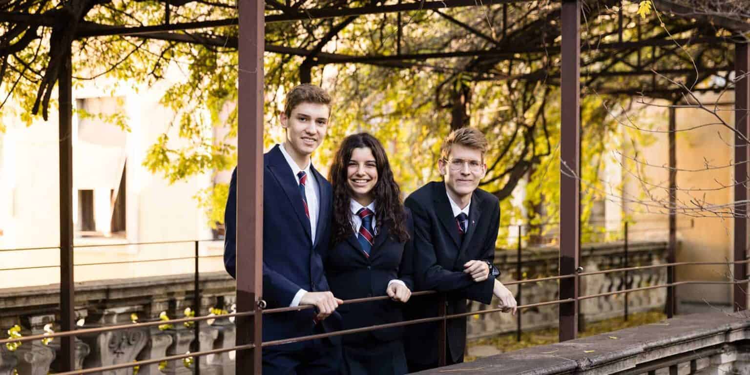 High school students in uniform smiling outdoors, autumn foliage background, emphasizing education and community.