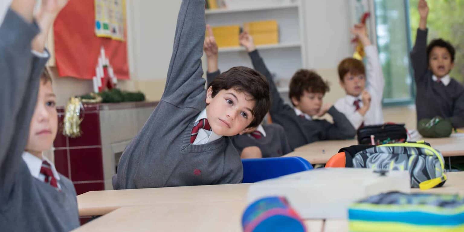 Bright classroom of diverse students actively participating, raising hands, and engaged in learning.