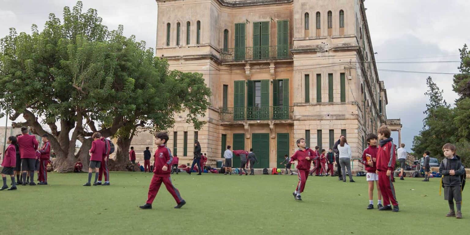 Children outdoor school yard playing under trees at historic building optima international school.