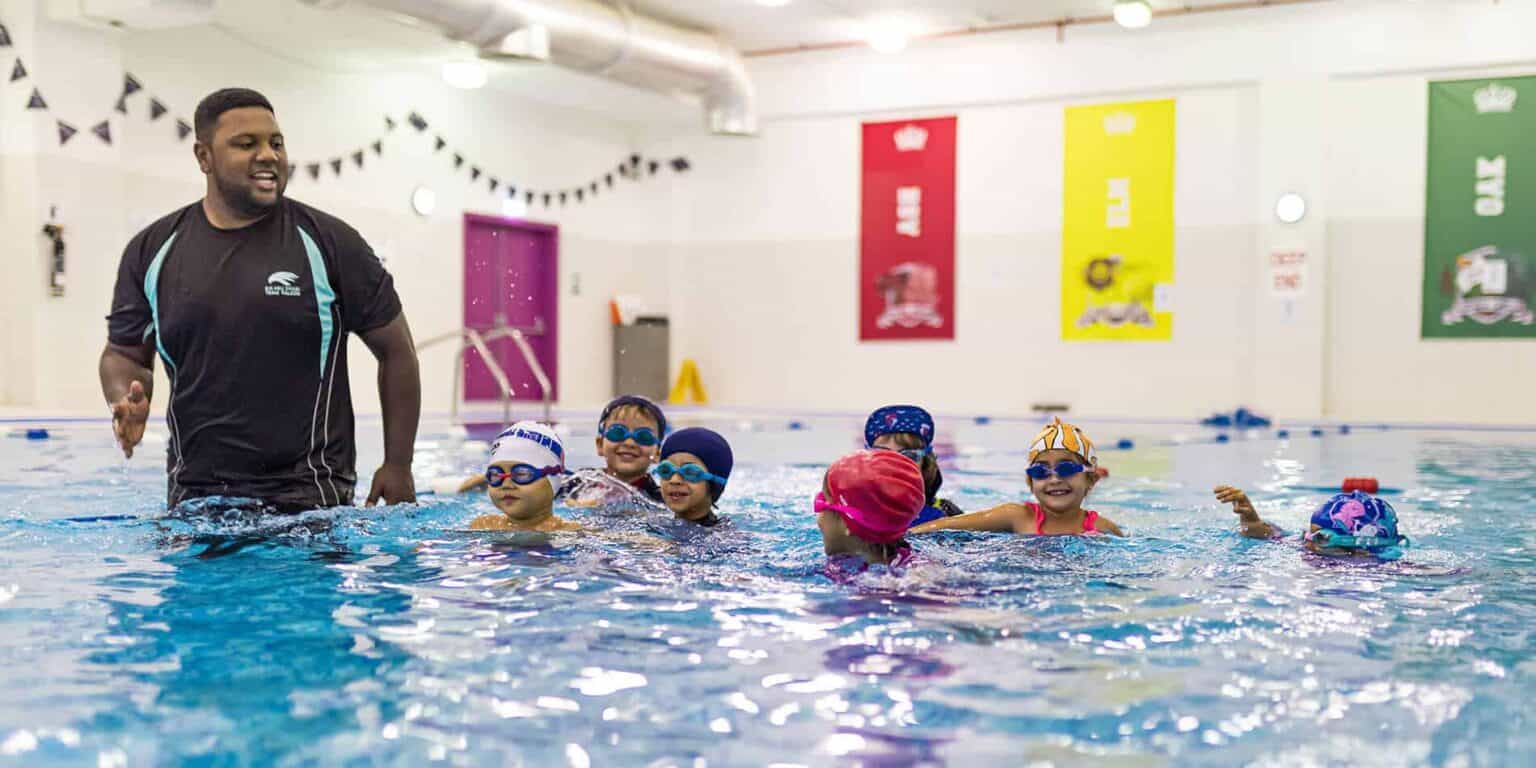 Niños nadando en piscina cubierta con instructor, promoviendo la educación sobre seguridad en el agua en los Colegios del Mundo.