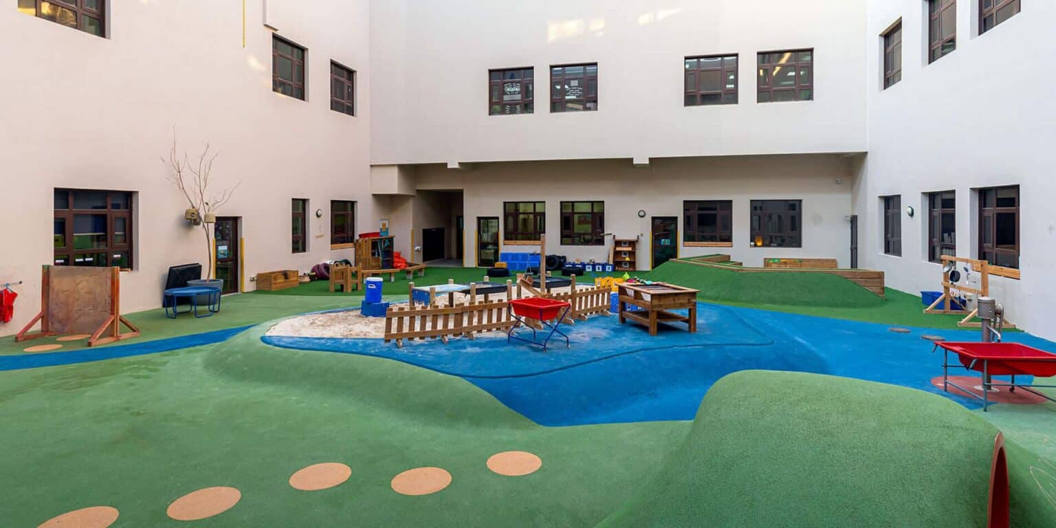 Luminoso patio de recreo al aire libre en un campus de los Colegios del Mundo, con vistosos juegos y césped artificial para el esparcimiento de los niños.