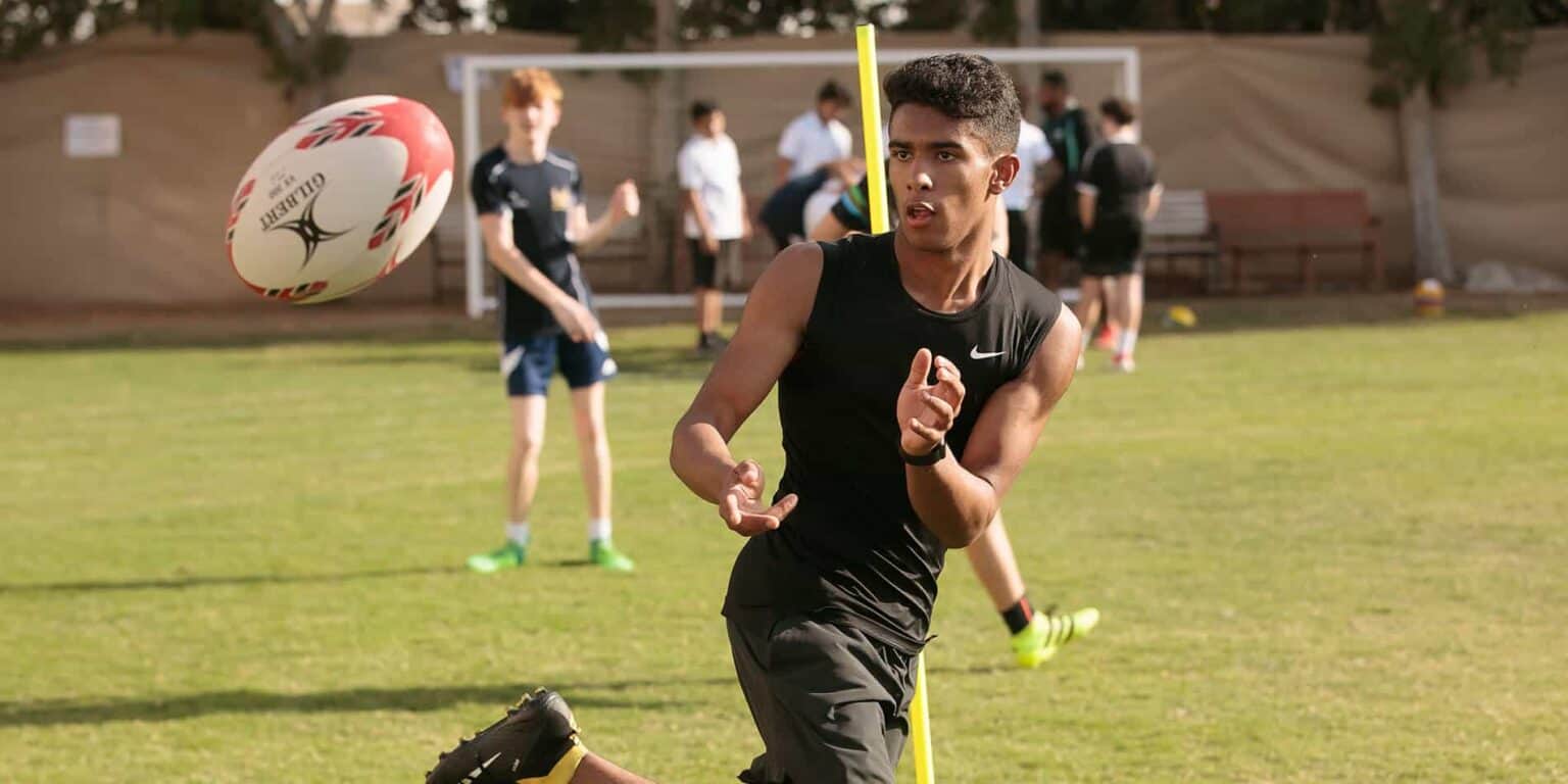 Joven atleta atrapando un balón de rugby durante una sesión de entrenamiento en un campo deportivo.