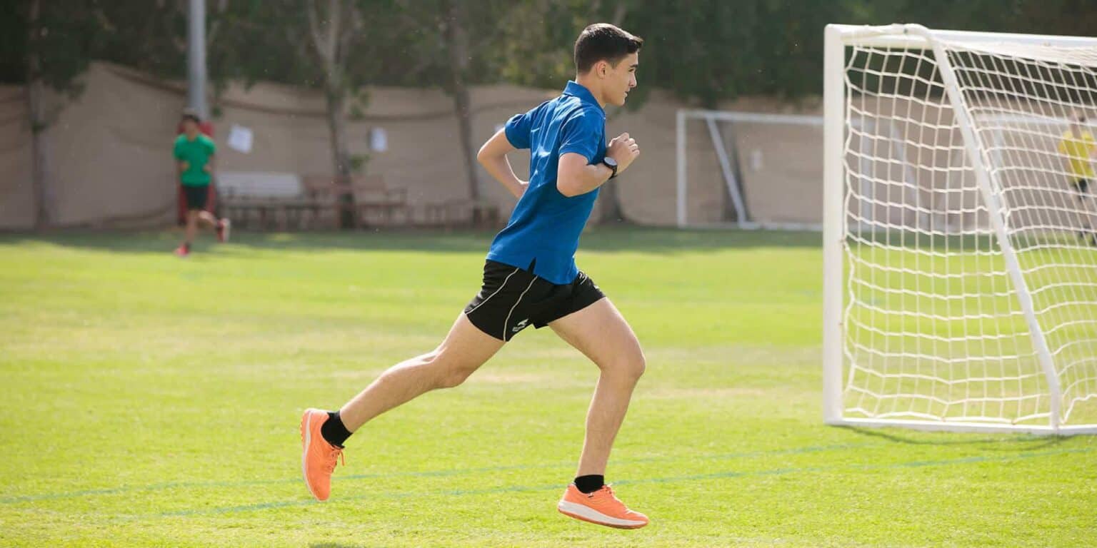 Adolescente activo corriendo en un campo de fútbol cerca de una portería en un evento deportivo de los Colegios del Mundo.