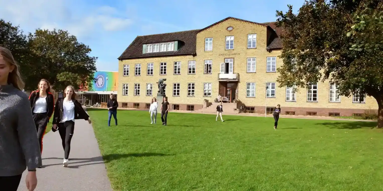 Students walking outside a historic school building in Germany, sunny day, educational campus, international schooling.