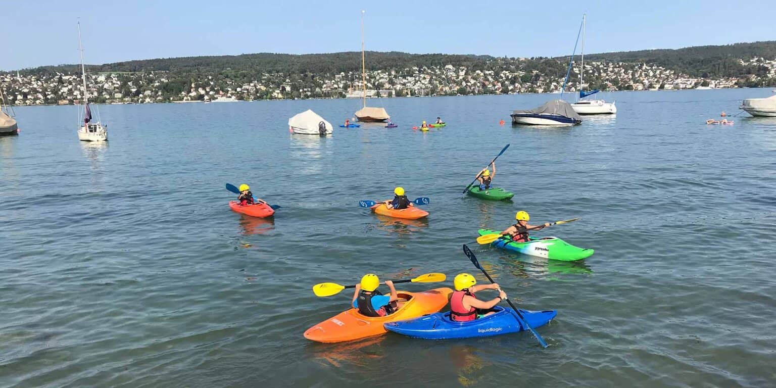 Children kayaking at a scenic lake during a school activity, promoting outdoor education and adventure sports.