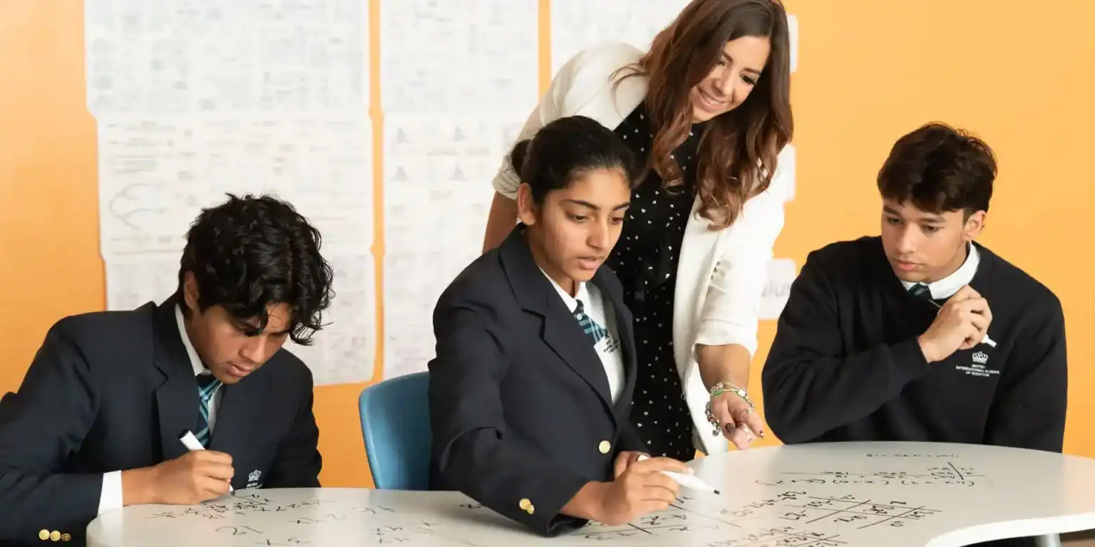 Diverse students collaborating on math problems in a classroom with teacher guidance, promoting international education excellence.