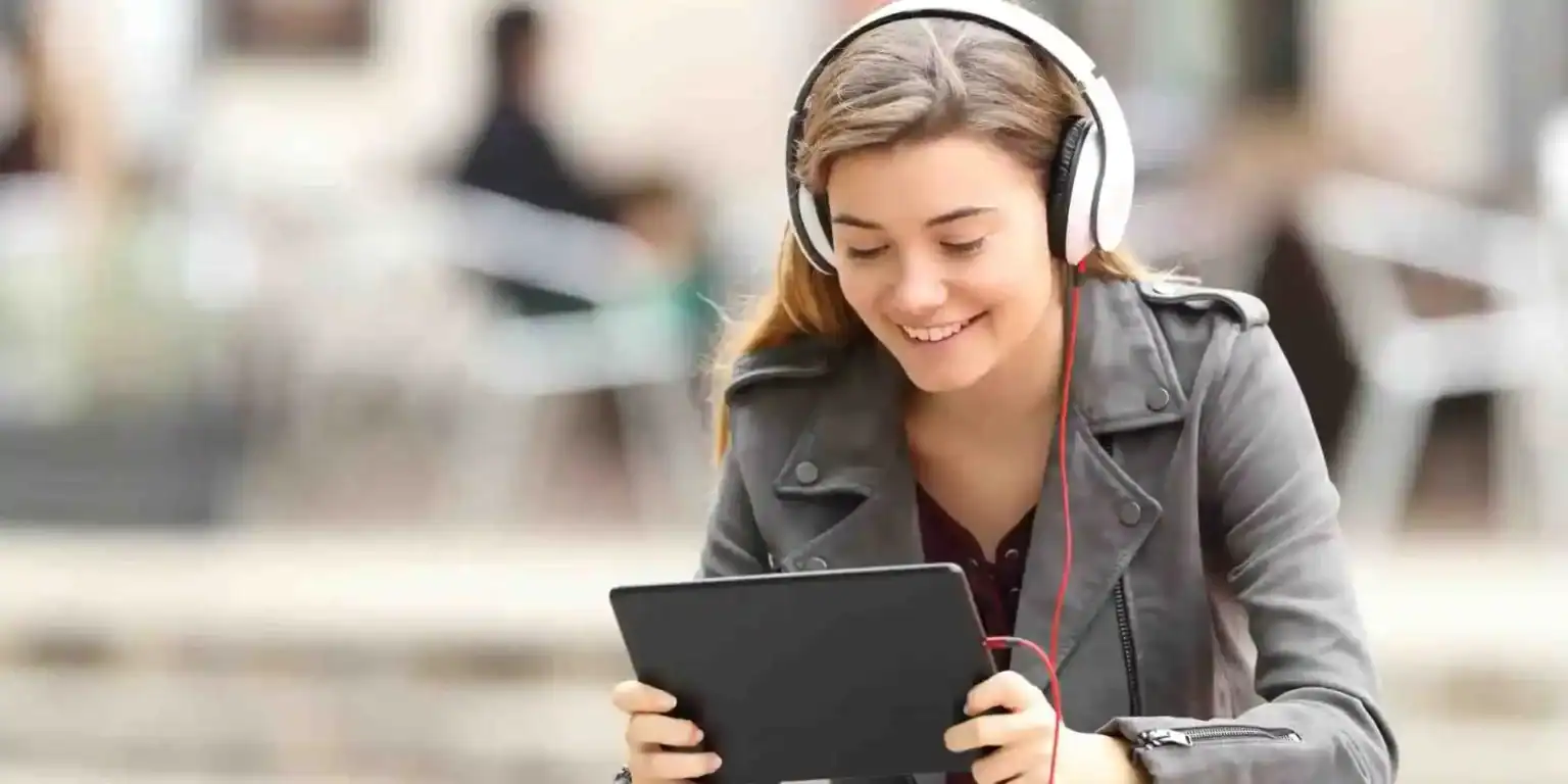 Young female student enjoying online learning with headphones and tablet in urban setting.