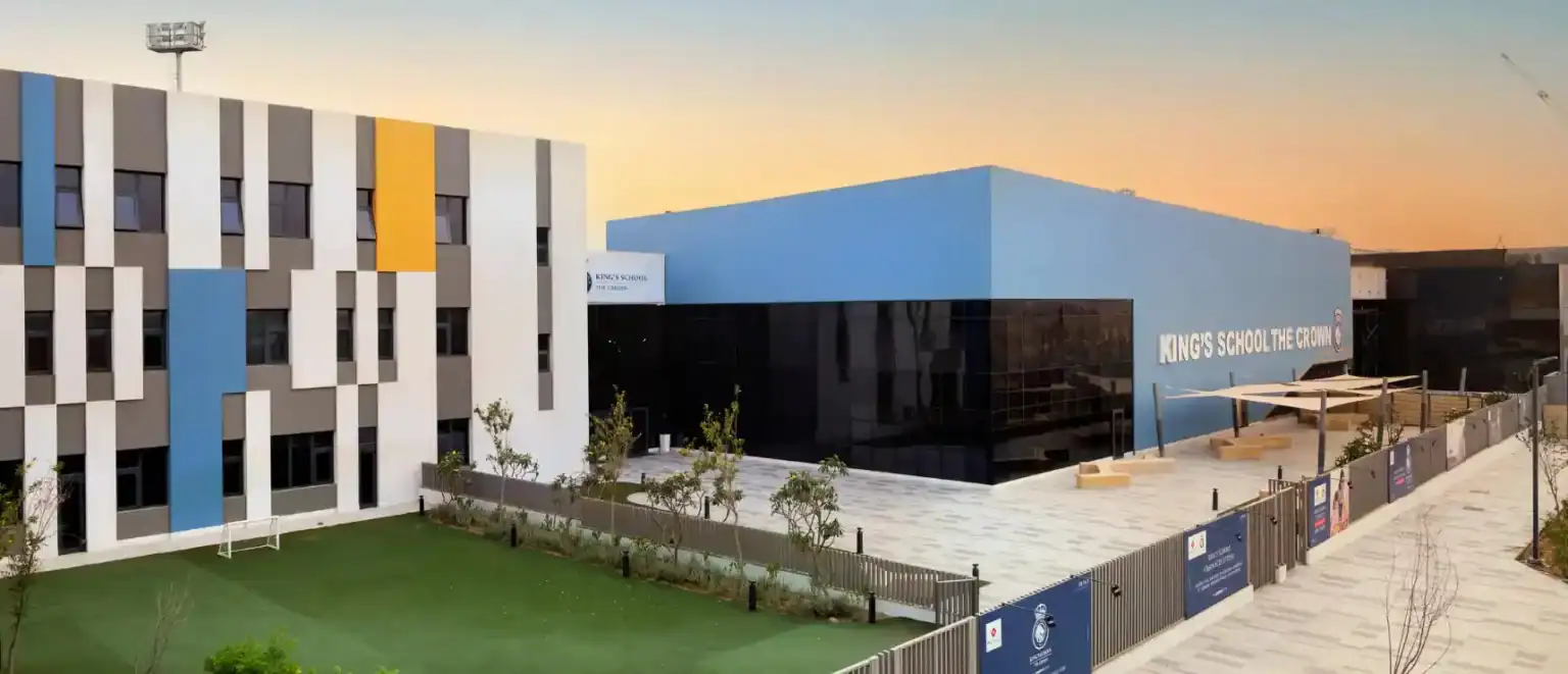 Modern Kings School building exterior with colorful facade, sports field, and sunny sky, fostering a conducive learning environment.