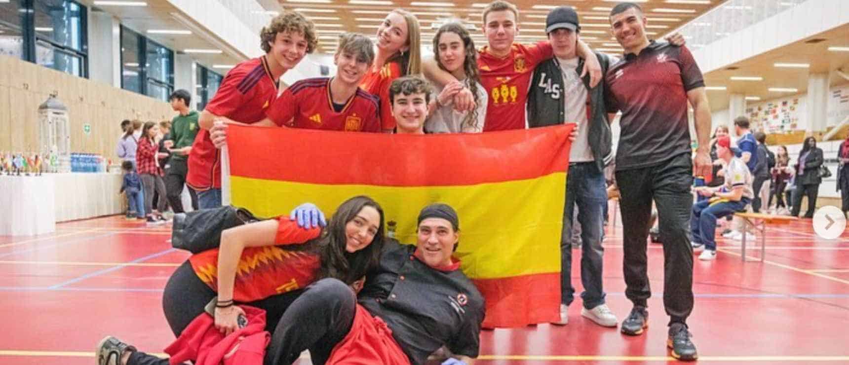Youth soccer team holding Spanish flag at an indoor sports event, celebrating victory and teamwork.