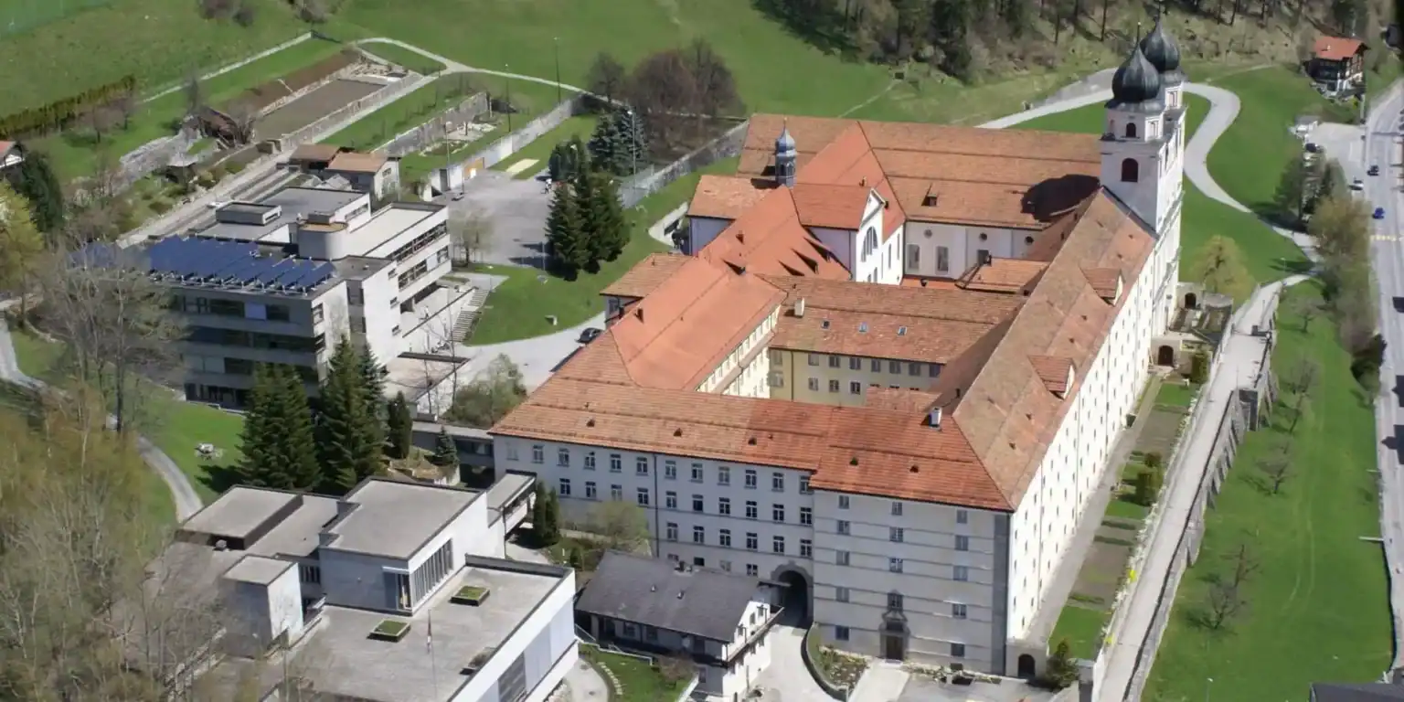 Ancient monastery with red-tiled roofs and modern educational facilities amidst lush greenery.