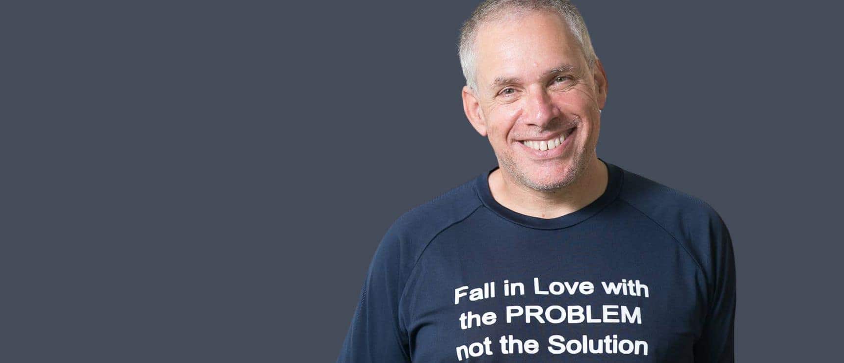 Motivational speaker wearing a "Fall in Love with the PROBLEM" T-shirt, smiling confidently.