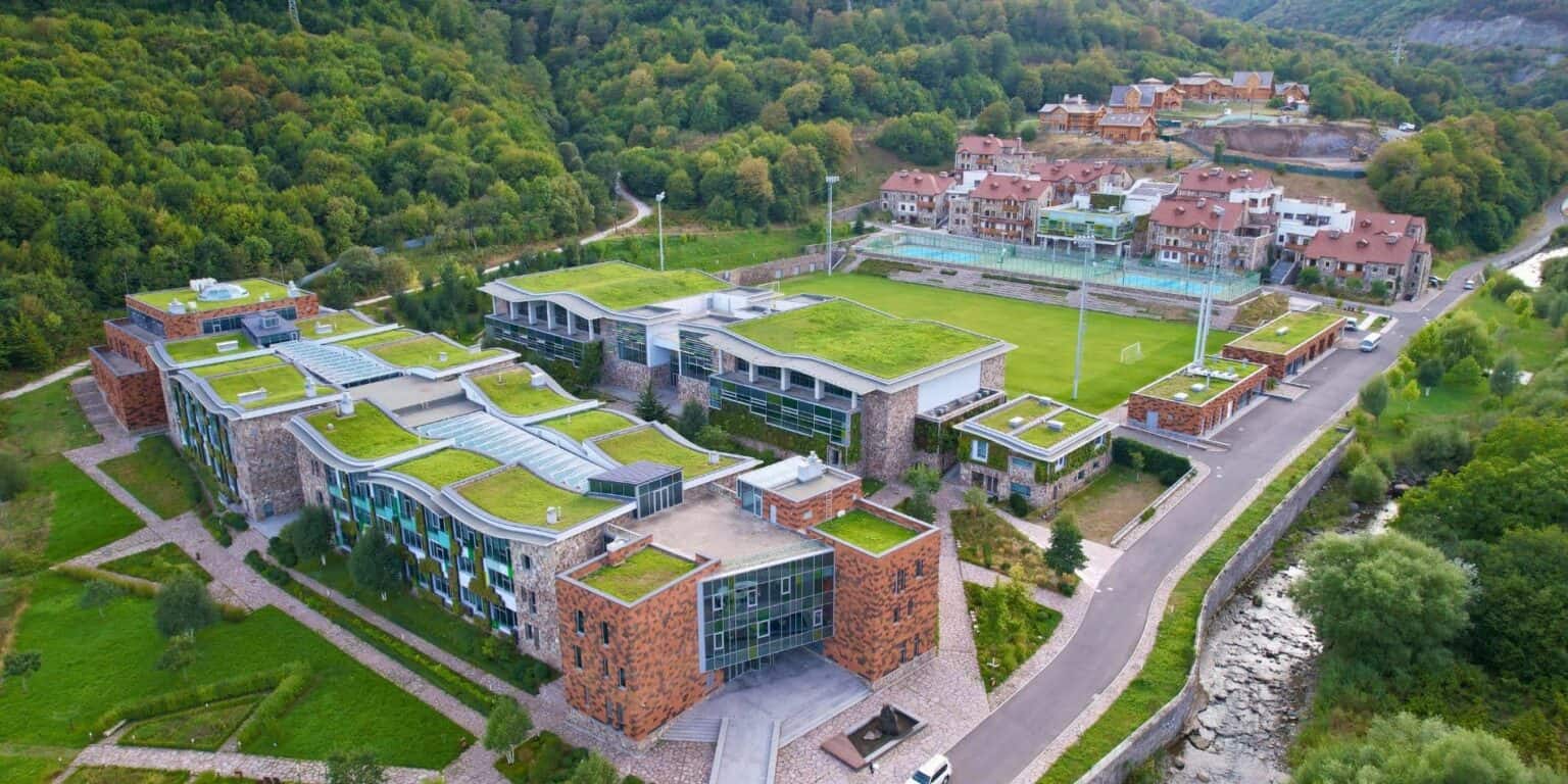 Modern international school campus with green roofs in lush mountain setting.