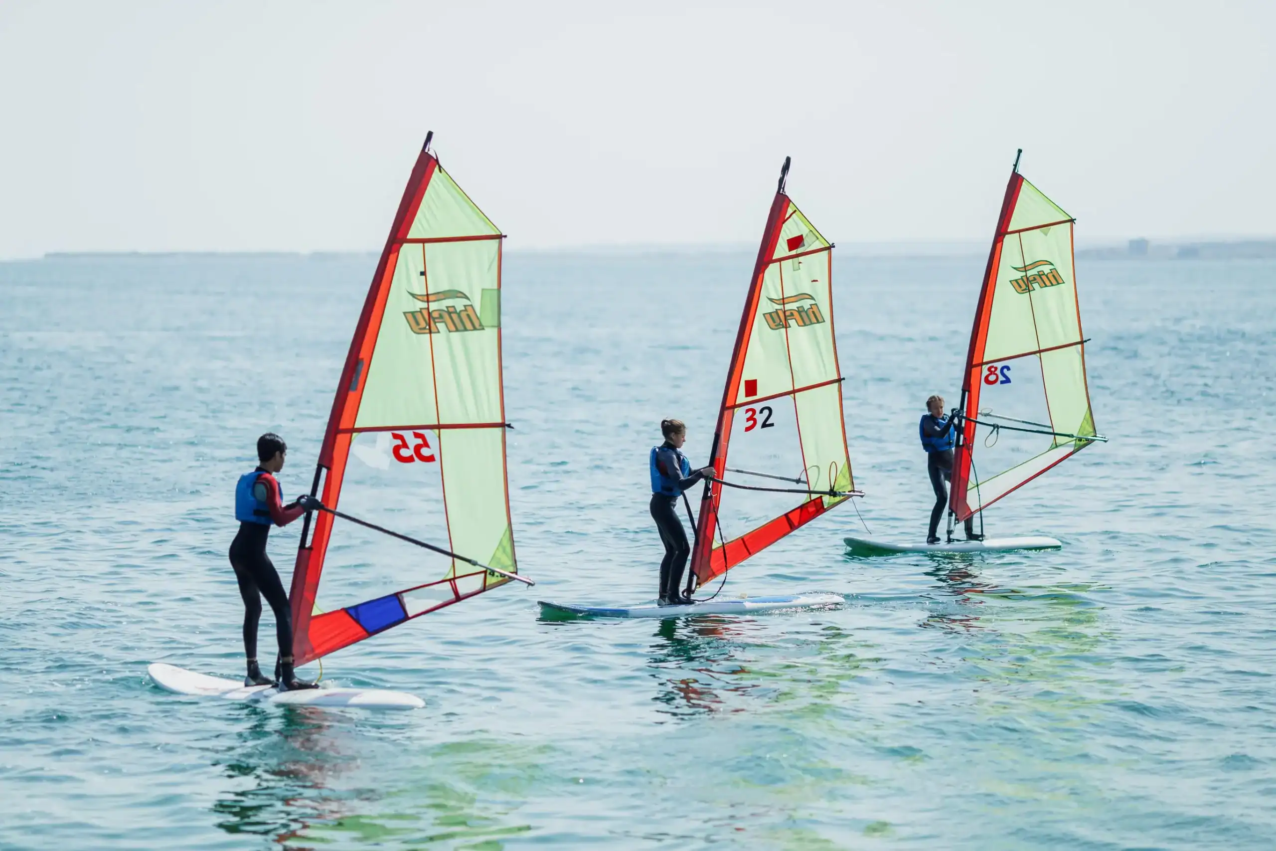 Little kids windsurfing on the ocean, learning water sports at a World School.
