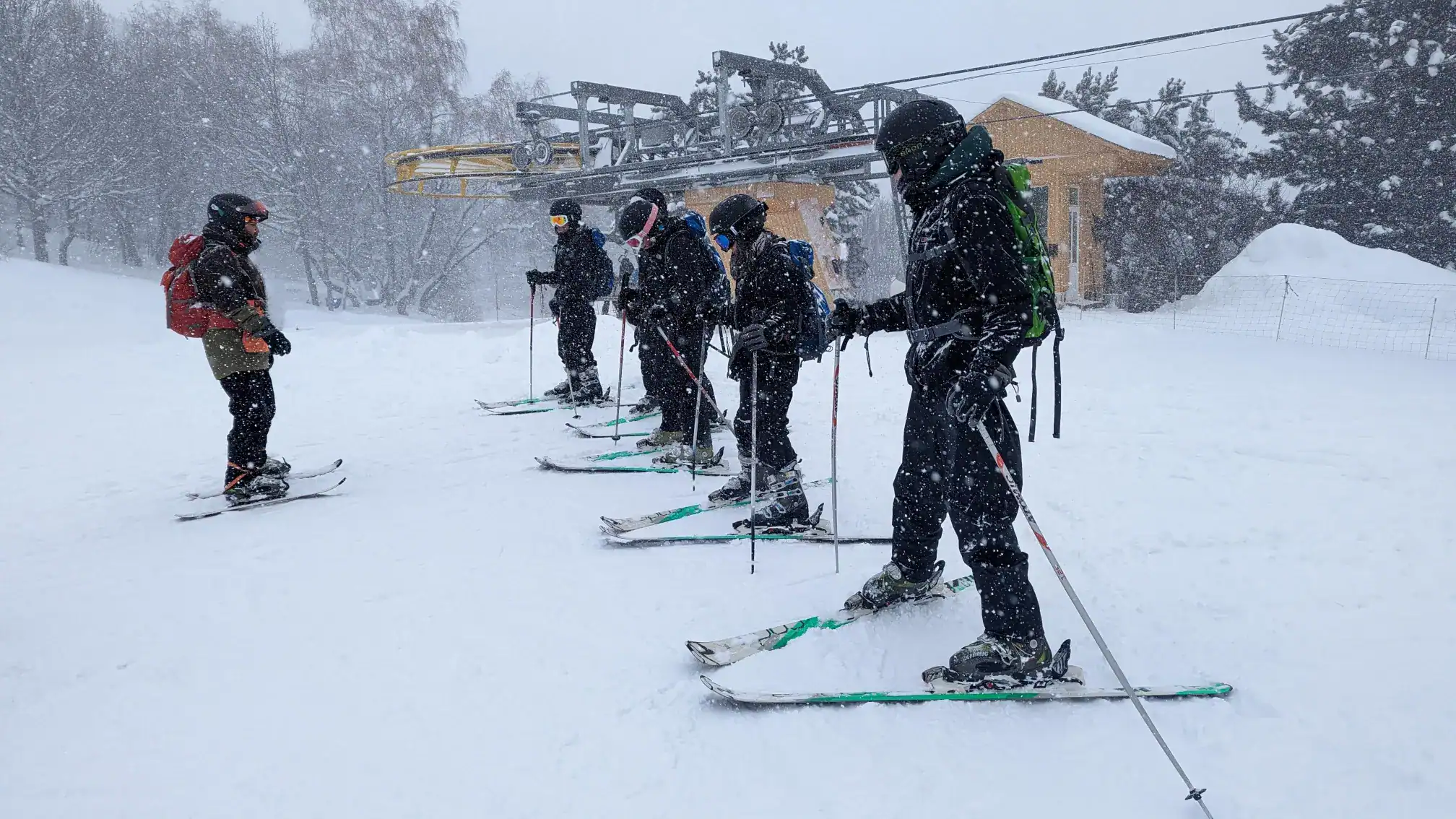 Skiers in snowy mountain resort preparing for ski lesson during snowstorm.