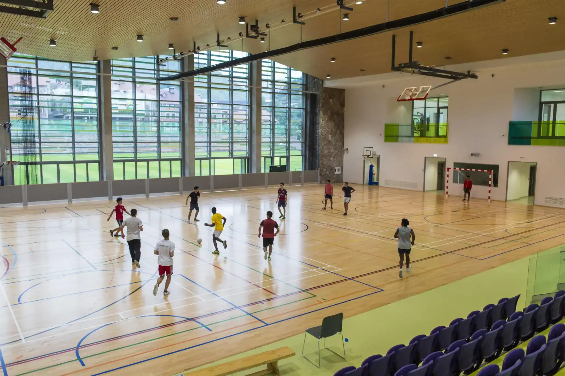 Bright indoor gymnasium with students playing football, large glass windows, and modern sports facilities for world schools.