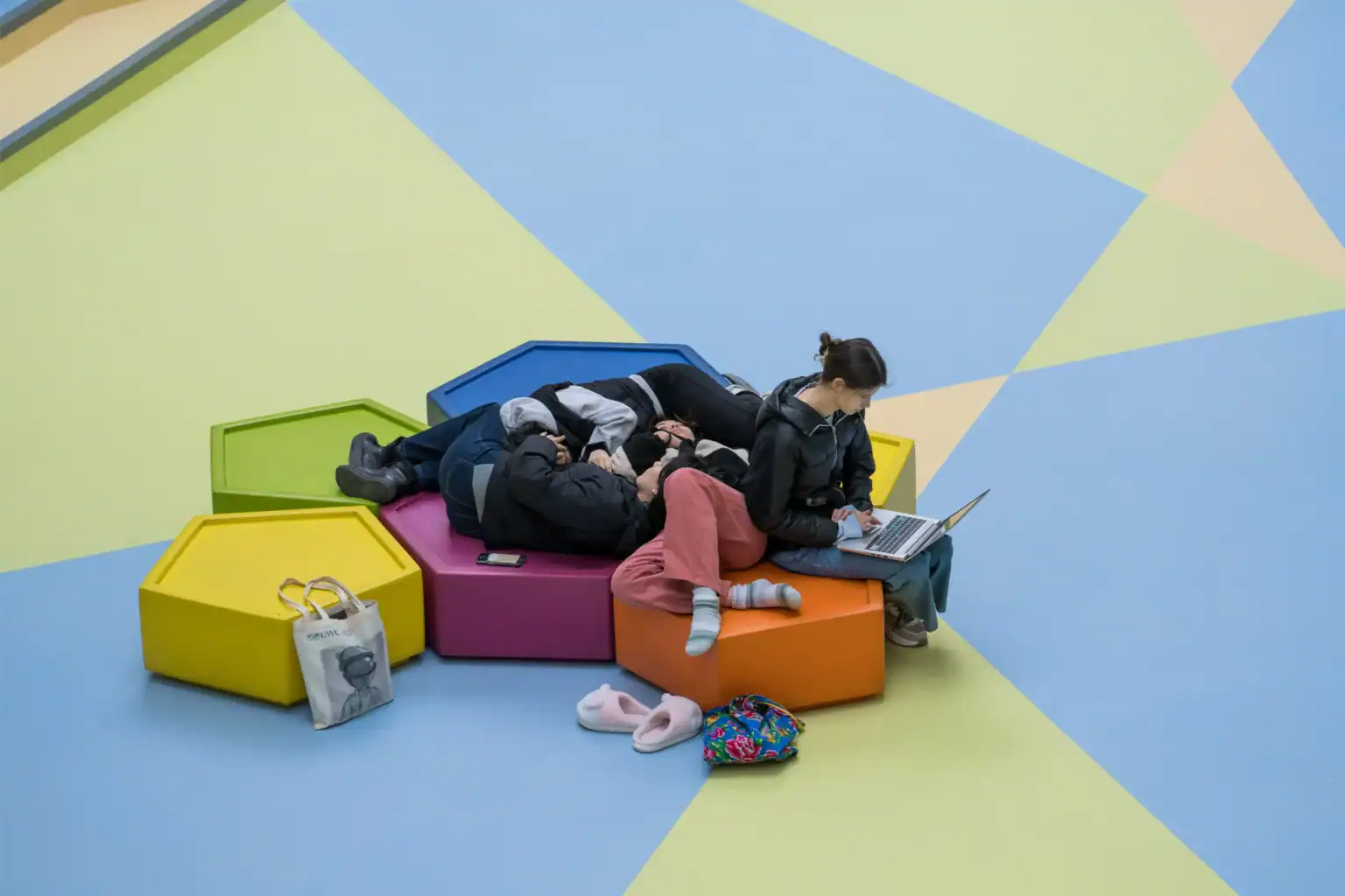 Colorful modern school lounge with students using laptops and resting on vibrant geometric seating.