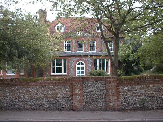 Historic brick school building with large windows and trees in front.