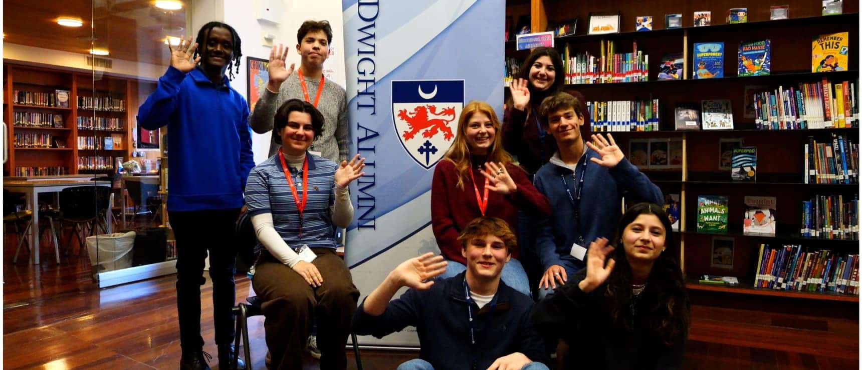 Diverse group of students waving at the camera in a library at World Schools, promoting international education.