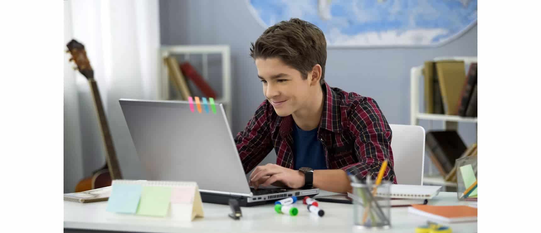 Young student working on a laptop in a bright, modern classroom with educational materials.