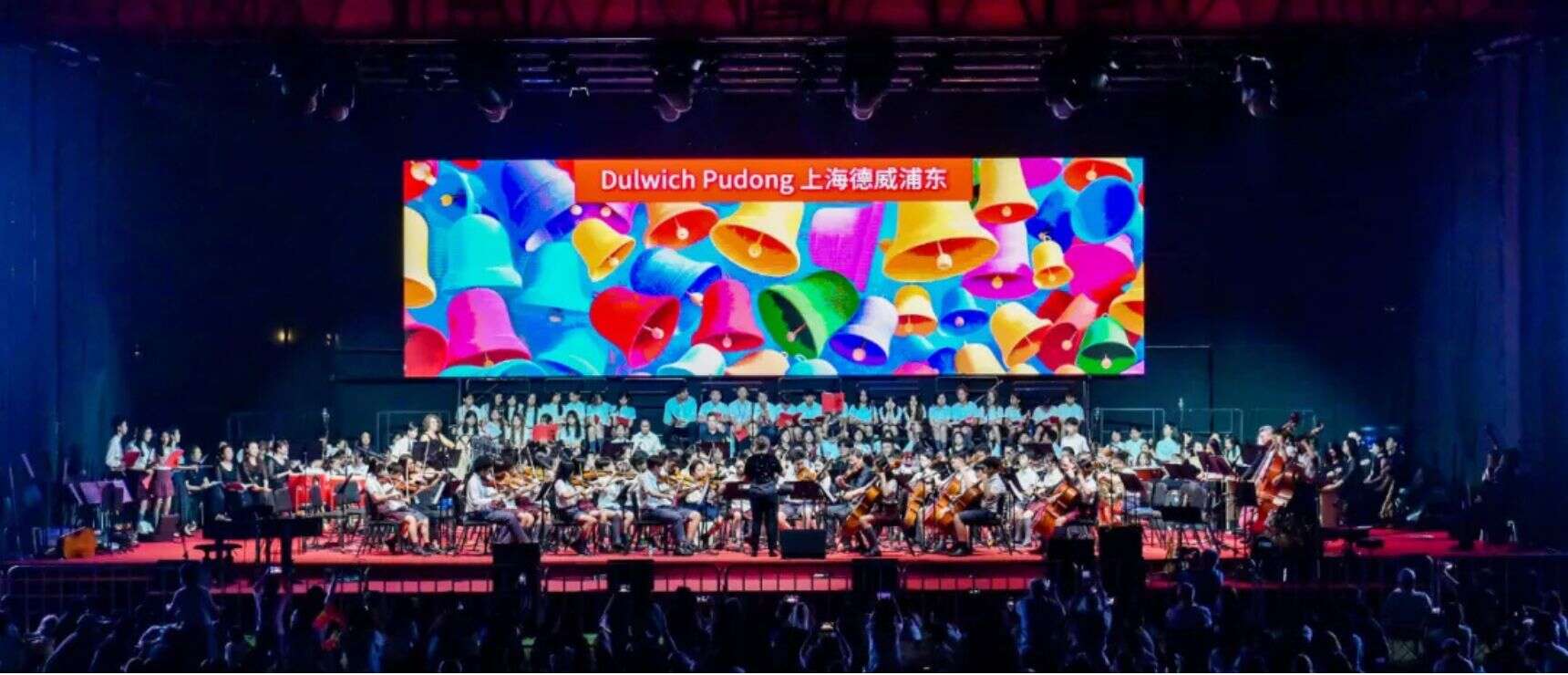 Colorful bells digital display at a school concert hall with orchestra performing on stage.
