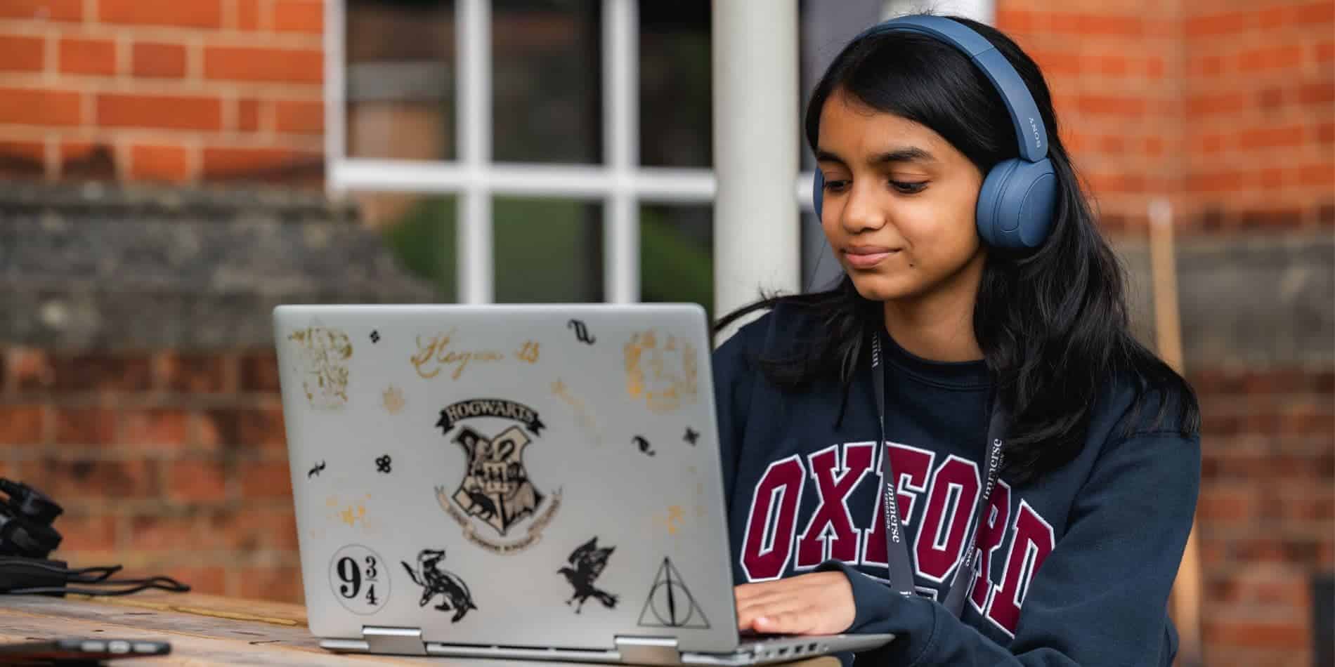 Young girl with headphones studying at laptop, outdoor educational environment.